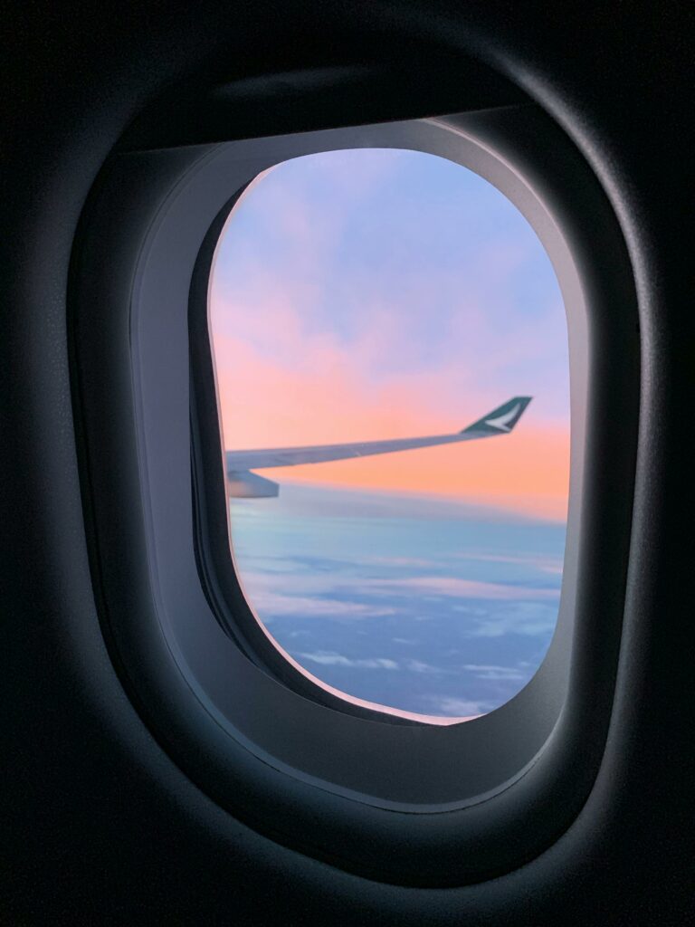 Airplane window view of wing and colorful sunset sky during flight.